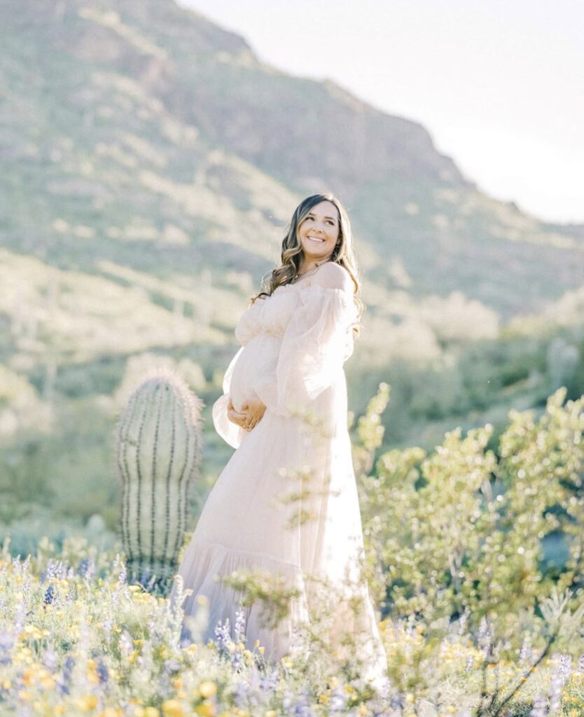 Pregnant mother glowing in the desert sun during Nest: A Luxury Maternity & Newborn Workshop, her tulle dress catching the light in a dreamy, radiant scene.
